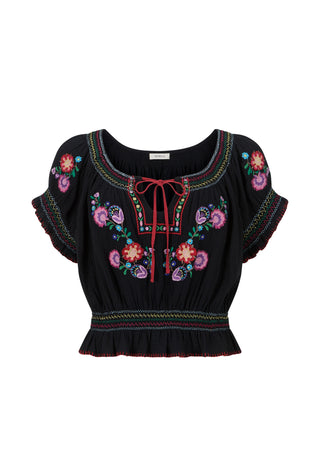 A close-up of a woman wearing a black bohemian-style blouse with colorful floral embroidery and a red tie-neck detail