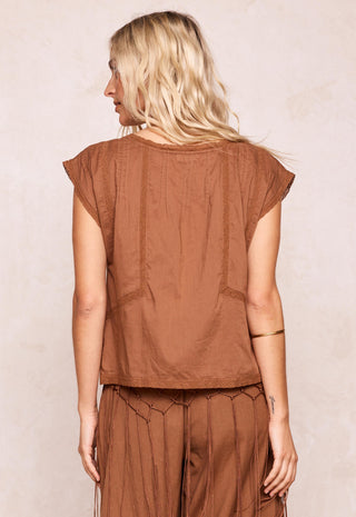 a-woman-shown-from-the-back-wearing-a-brown-short-sleeve-top-and-matching-brown-pants-against-a-light-beige-textured-wall