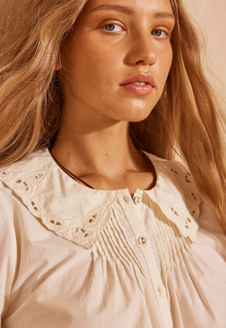 a-close-up-shot-of-a-woman-wearing-a-cream-colored-blouse-with-a-large-eyelet-lace-peter-pan-collar-and-smocked-detailing-on-the-chest