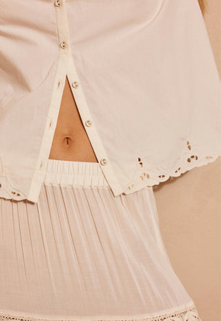 a-close-up-of-a-woman-modeling-a-cream-colored-short-sleeve-bohemian-style-blouse-and-matching-skirt-against-a-warm-beige-background