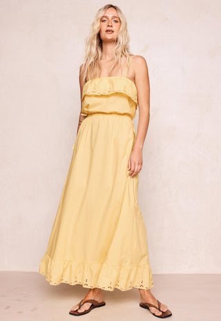 a-woman-modeling-a-pale-yellow-strapless-maxi-dress-with-ruffle-details-paired-with-brown-sandals-standing-against-a-textured-beige-wall