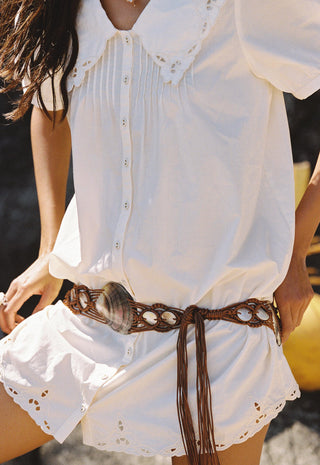 a-close-up-of-a-person-wearing-a-white-short-sleeve-blouse-and-matching-white-shorts-with-eyelet-lace-trim-styled-with-a-brown-woven-belt