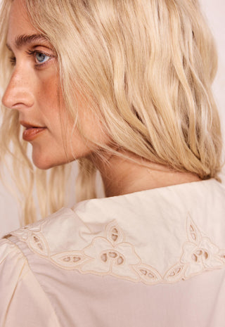 close-up-of-a-woman-with-blonde-hair-wearing-a-cream-colored-blouse-with-a-large-embroidered-collar