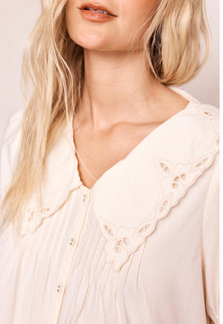 close-up-of-a-woman-wearing-a-cream-colored-blouse-with-a-large-eyelet-peter-pan-collar-and-button-front