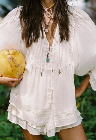 a-woman-wearing-a-loose-white-bohemian-style-blouse-with-ruffled-trim-and-front-buttons-holding-a-yellow-coconut-outdoors