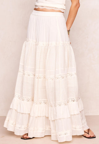 a-long-tiered-white-maxi-skirt-with-delicate-lace-trim-and-horizontal-textured-bands-shown-on-a-model-against-a-light-beige-textured-wall