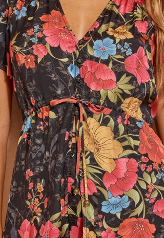 a-close-up-shot-of-a-woman-modelling-a-short-sleeve-floral-mini-dress-with-a-lace-hem-standing-against-a-textured-beige-wall