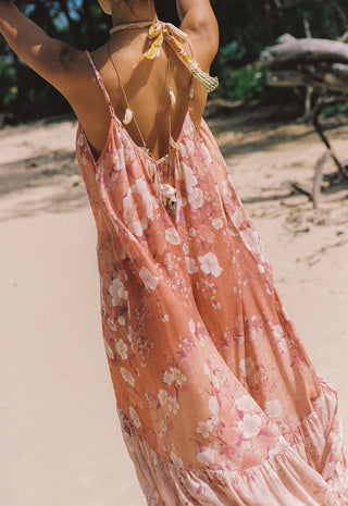 a-woman-on-a-sandy-beach-wearing-a-peach-pink-floral-halter-maxi-dress-shown-from-behind