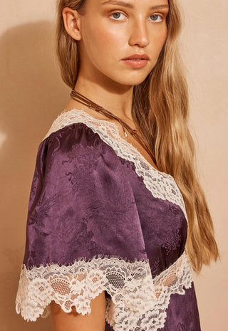 a-woman-wearing-a-purple-satin-slip-dress-with-white-lace-trim-photographed-against-a-warm-beige-background