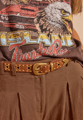 a-close-up-of-a-person-wearing-a-brown-graphic-t-shirt-with-an-eagle-and-car-print-paired-with-a-brown-studded-belt-and-brown-pleated-pants