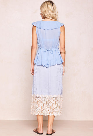 a-woman-shown-from-the-back-wearing-a-light-blue-ruffled-midi-dress-with-a-lace-hem-standing-against-a-neutral-beige-wall