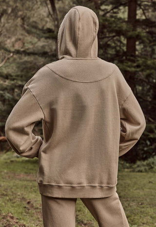 a-person-viewed-from-behind-wearing-a-matching-beige-hooded-sweatshirt-and-jogger-pants-in-an-outdoor-wooded-setting