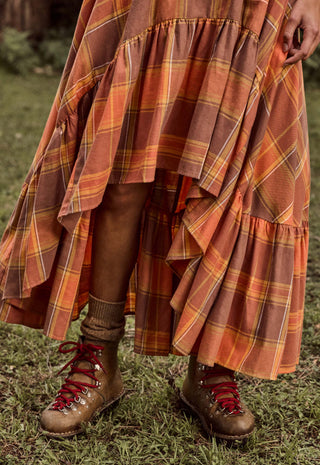 a-close-up-outdoor-shot-of-a-person-wearing-a-long-tiered-plaid-skirt-in-rust-orange-brown-and-yellow-tones-paired-with-brown-lace-up-hiking-boots-on-grass