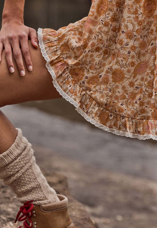 close-up-of-a-person-wearing-a-tan-and-brown-floral-skirt-with-a-white-lace-hem-paired-with-beige-knit-leg-warmers-and-brown-boots-with-red-laces